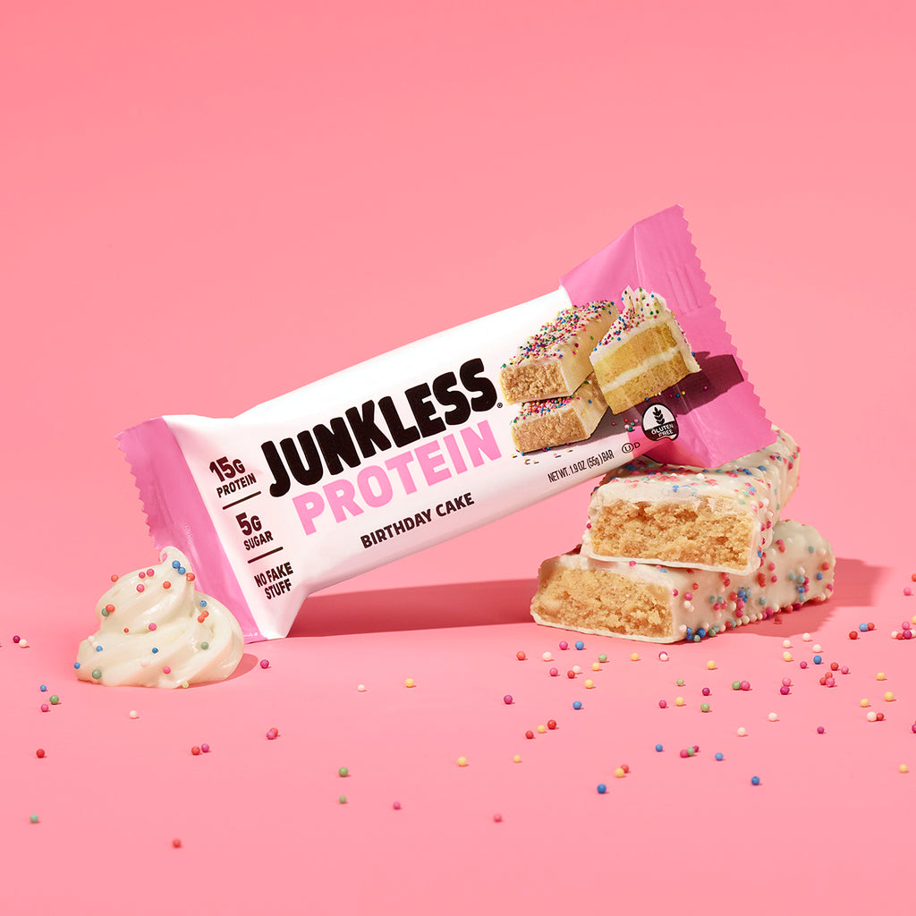 Junkless Protein Birthday Cake flavor bar on a pink background with sprinkles.