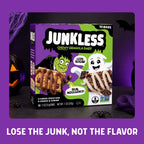A box of Junkless Chewy Granola Bars displayed on a dark surface with Halloween-themed props, including a jack-o'-lantern, spiderwebs, and spiders, against a purple background. The box is purple and green with cartoon graphics of Frankenstein and a ghost, and the text 'LOSE THE JUNK, NOT THE FLAVOR' is written at the bottom.