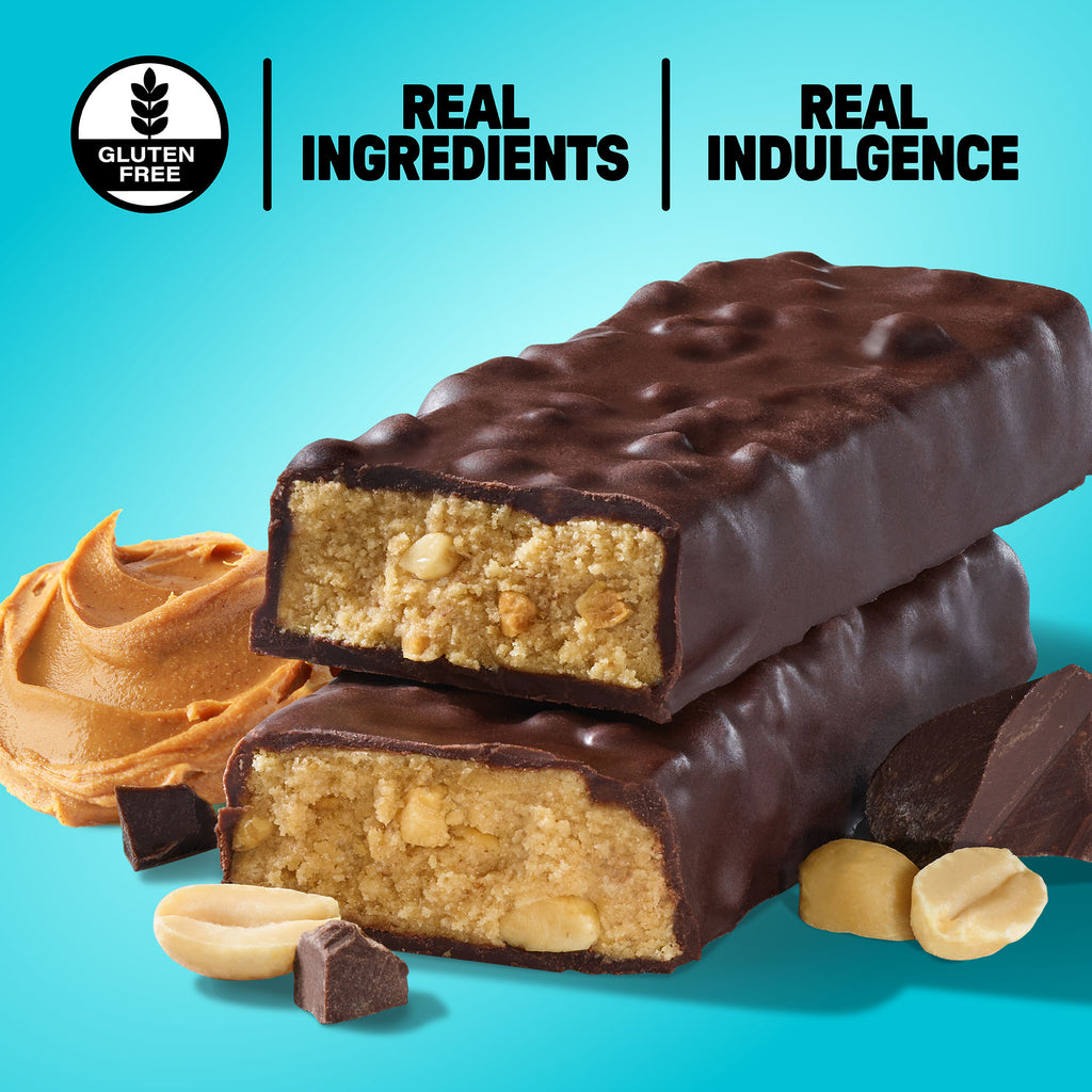 An unwrapped chocolate covered protein bar with a smear of peanut butter, chocolate chunks and peanuts on a blue background