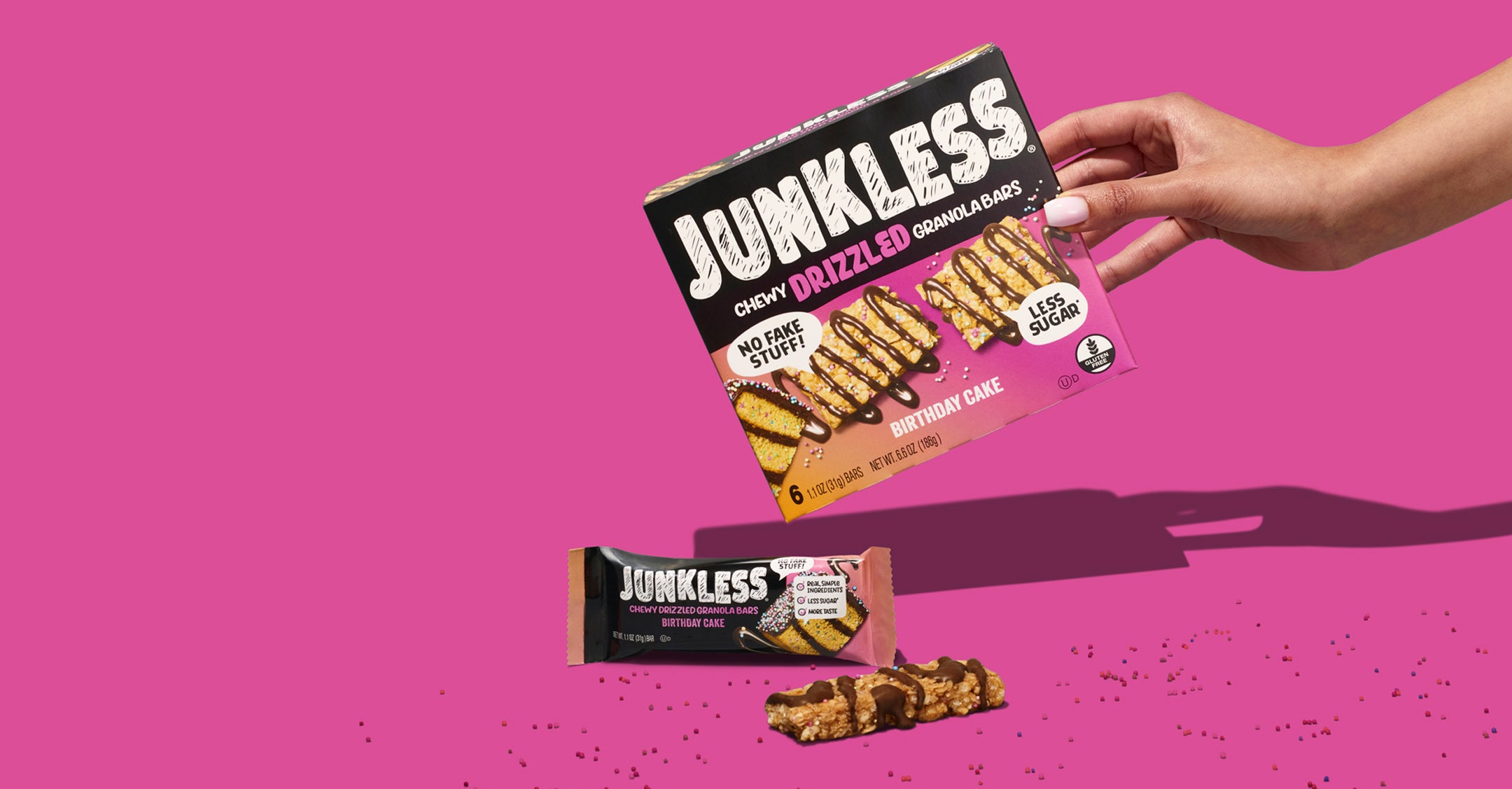Junkless granola bar packaging with a hand holding it against a pink background