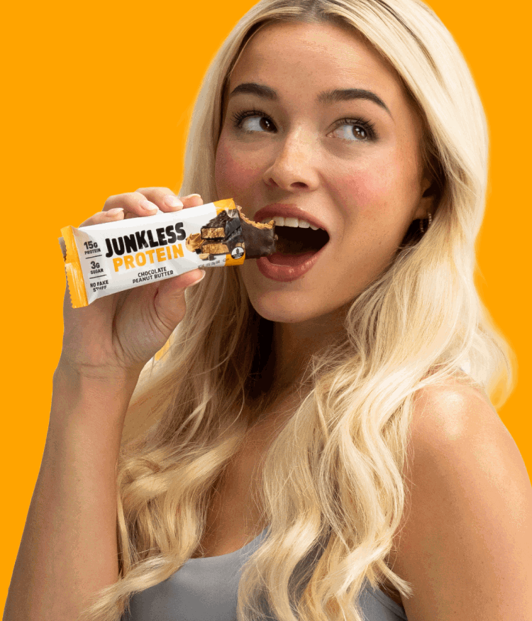 Livvy Dunne eating a Chocolate Peanut Butter Protein Bar on an orange background.